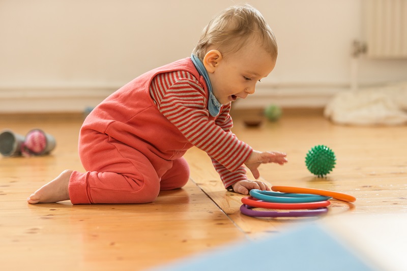 Baby im Vierfüßlerstand greift nach bunten Ringen.