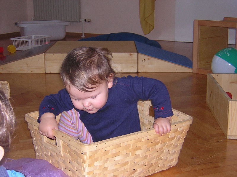 Kleinkind sitzt in einem kleinen Korb und will gerade aufstehen