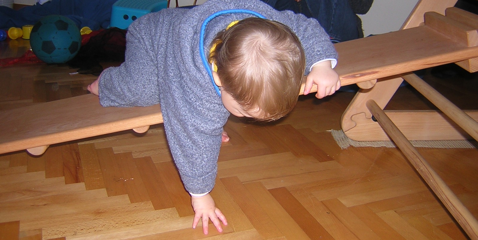 Baby klettert kopfüber über eine Rutsche. Sie stützt sich dabei mit der rechten Hand ab.