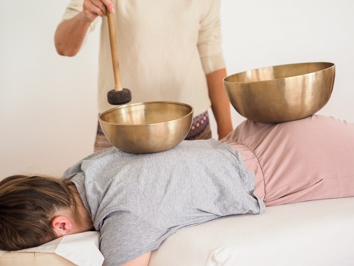 Eine Frau liegt auf dem Bauch, auf ihrem Rücken werden Klangschalen zum Klingen gebracht.