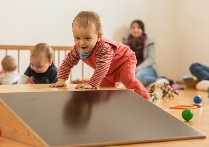 Im Pikler-SpielRaum. Ein Baby stützt sich am Holzpodest auf und steht.
