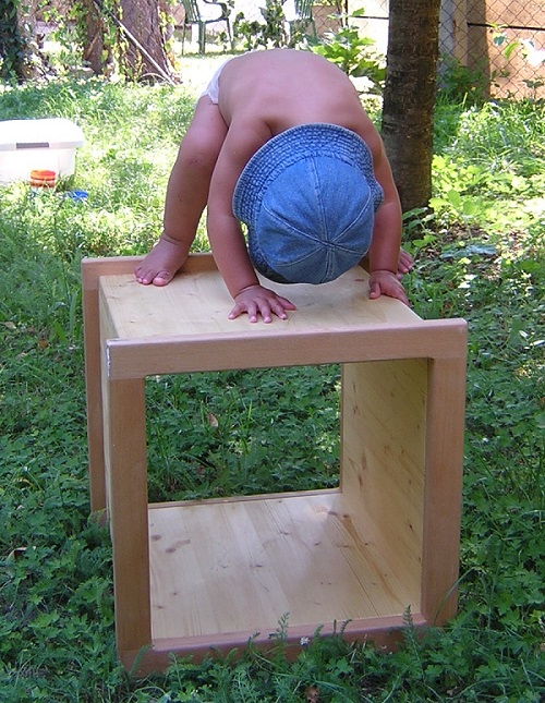Kleinkind steht mit allen Vieren auf einem Holzwürfel