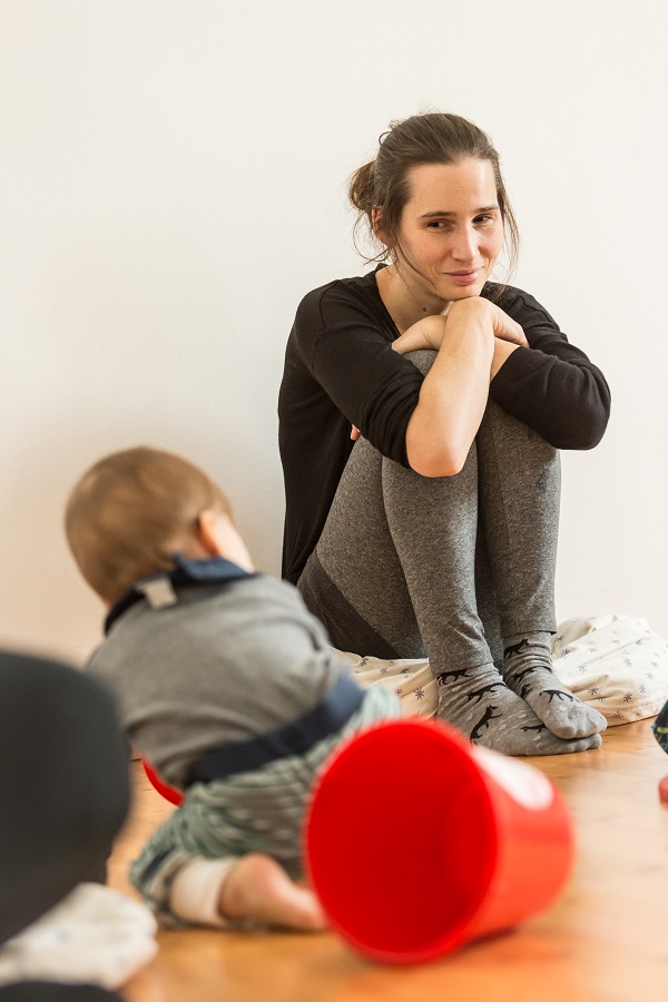 Im Pikler-SpielRaum: Eine Mutter sitzt am Boden und sieht ihrem Baby beim Krabbeln zu.