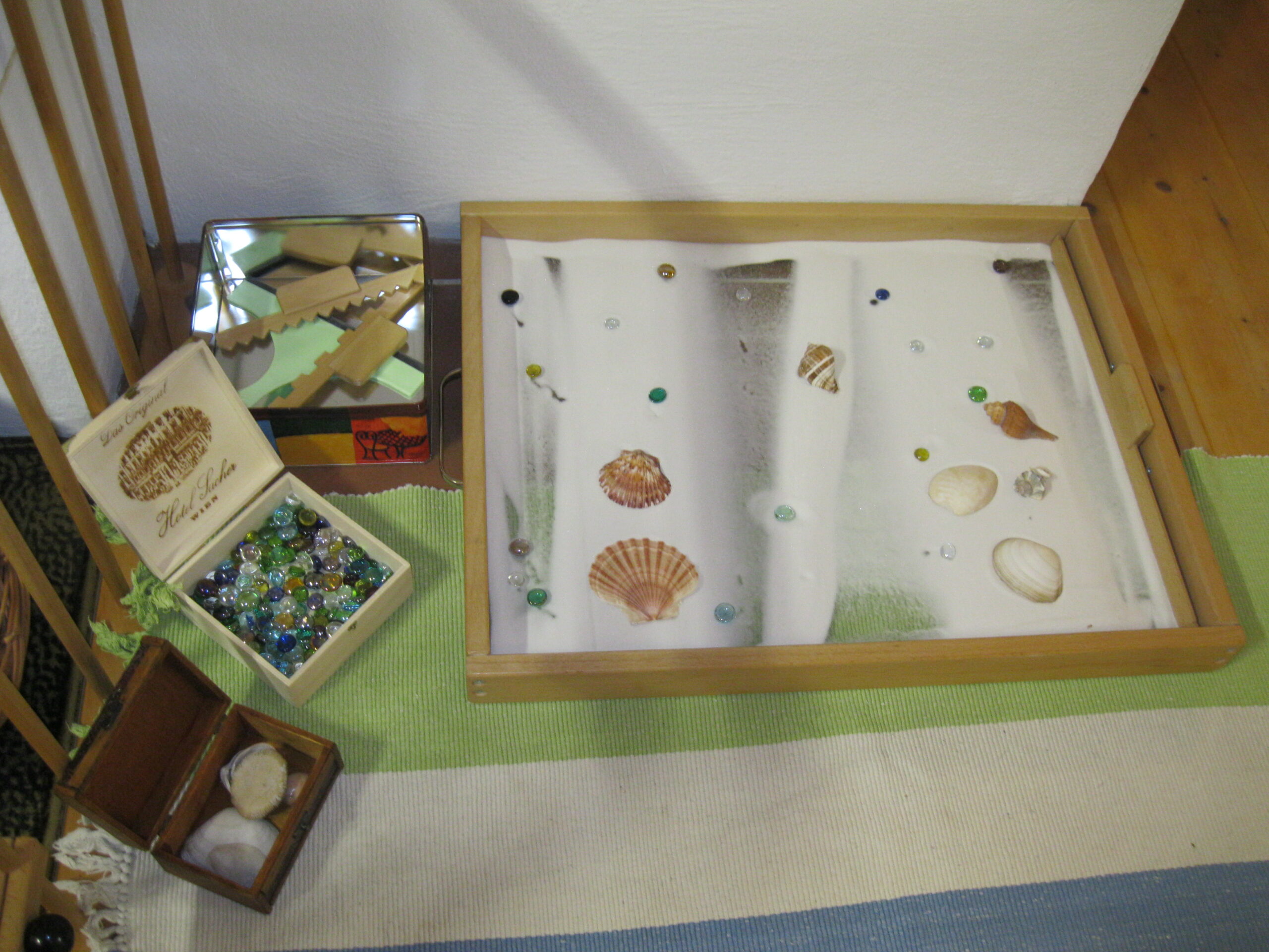 Sandwanne mit feinem weißem Sand. Spiel-und Zeichenzubehör wie Muscheln, Glasnuggets und Holzschaber